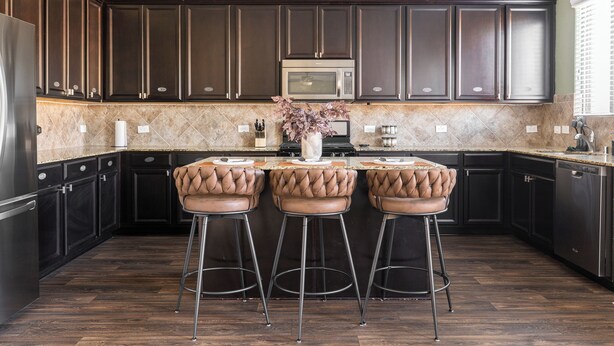 A modern kitchen with dark wood cabinets, a central island with bar stools, a stainless steel refrigerator, and a microwave. - Giddyup Getaway: Western Oasis w/ Pool! 4bd 9 beds (Cypress)