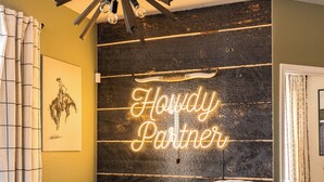 A dining area with a wooden table set for four, a neon sign reading "Howdy Partner", and a framed artwork on the wall. - Giddyup Getaway: Western Oasis w/ Pool! 4bd 9 beds (Cypress)