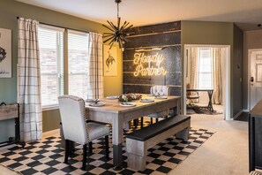 A dining area with a checkered floor, a wooden table, and white upholstered chairs.