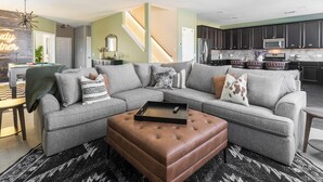 A modern living room with a sectional sofa, a brown ottoman, and a pool table. - Giddyup Getaway: Western Oasis w/ Pool! 4bd 9 beds (Cypress)