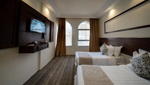 Ein Hotelzimmer mit zwei Betten, einem an der Wand montierten Fernseher und einem großen Fenster mit Vorhängen.