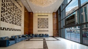 Eine geräumige Lobby mit modernem Design, ausgestattet mit einer großen Sitzecke mit blauen Sofas und einer Wand mit geometrischen Mustern.