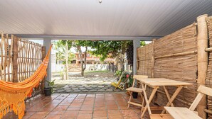 Alpendre coberto com rede, mesas de madeira e parede de bambu.