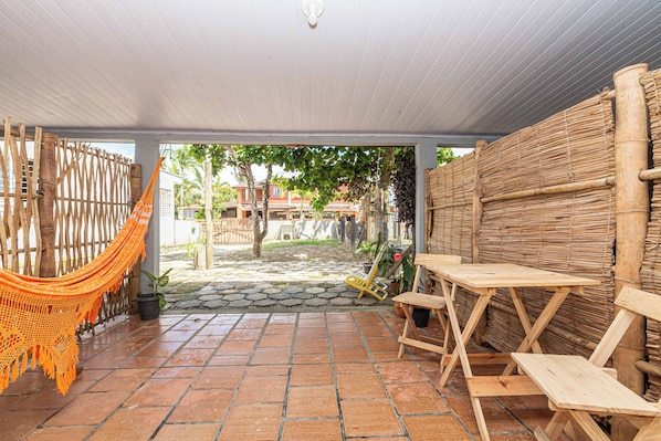 Une terrasse couverte avec un hamac, des tables en bois et un mur en bambou.