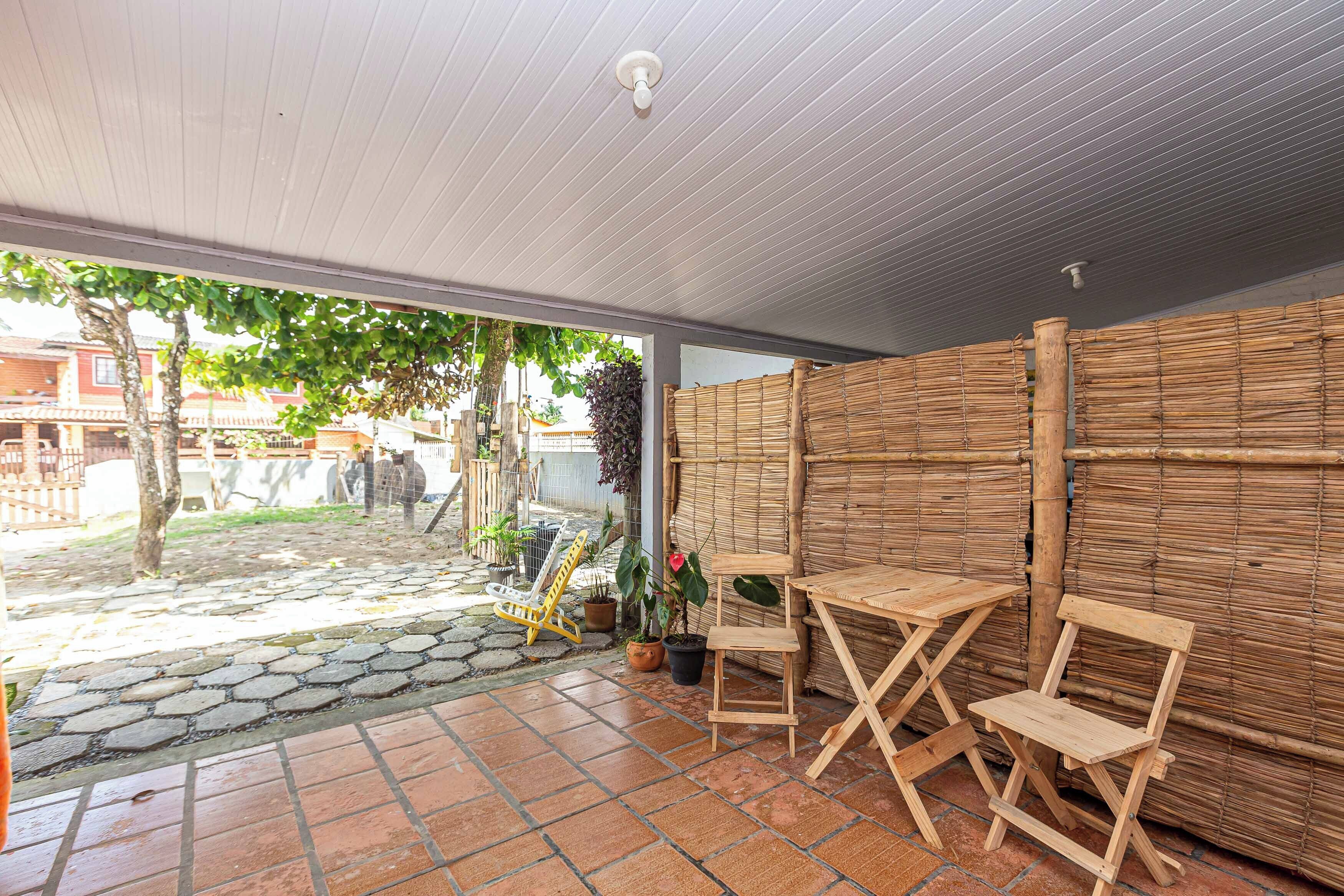 En overdækket terrasse med bambusafskærmninger, to træborde og krukker med planter.