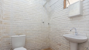 Casa de banho pequena, com azulejos brancos, incluindo sanita, lavatório e chuveiro.
