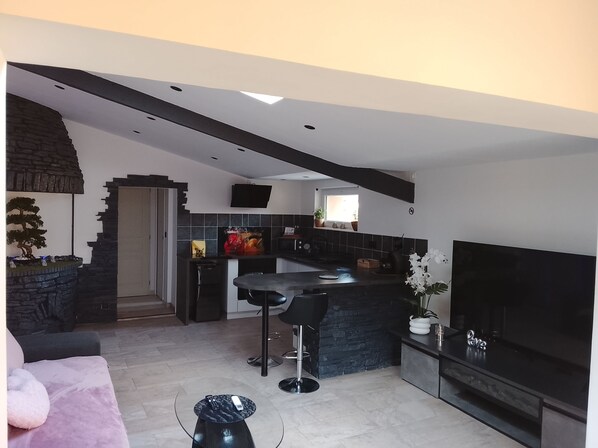 A modern kitchen with a stone island, black bar stools, and a large flat-screen TV.