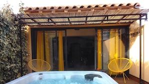 Een hottub met twee gele stoelen, een pergola en uitzicht op een gebouw met gele gordijnen.