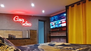 Een hotelkamer met een neonbord, een flatscreen-tv en een bed met een bloemenprint sprei.