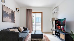 Een moderne woonkamer met een donkergrijze bank, een zwarte salontafel, een flatscreen televisie en een kamerbreed tapijt met een patroon.