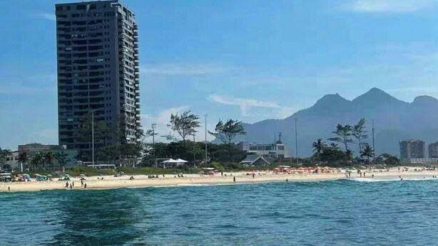 Un edificio alto cerca de la playa, con cielos despejados y montañas al fondo.