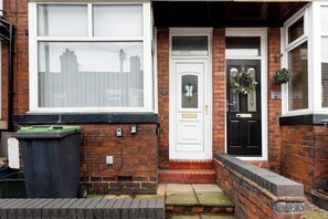 A residential property with a brick facade, a white front door, a number plate, and a green bin. - Spacious 4BR Home Near Alton Towers (Stoke-on-Trent)