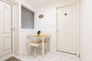 A small room with a white door marked with the number 4, a white table with two chairs, a window with a white curtain, and a small plant on the table. - Spacious 4BR Home Near Alton Towers (Stoke-on-Trent)