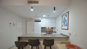 A modern kitchen with a central island, three bar stools, and a dining table with a red bowl.