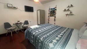 Ein Schlafzimmer mit einem Bett, einem Fernseher, einem Schreibtisch mit zwei Stühlen, einem Kleiderschrank und Wanddekorationen.