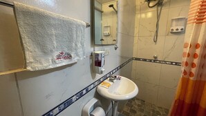 Ein Badezimmer mit weißem Waschbecken, einem Handtuch an der Wand, einer Dusche mit Duschbrause und einem Toilettenpapierhalter.