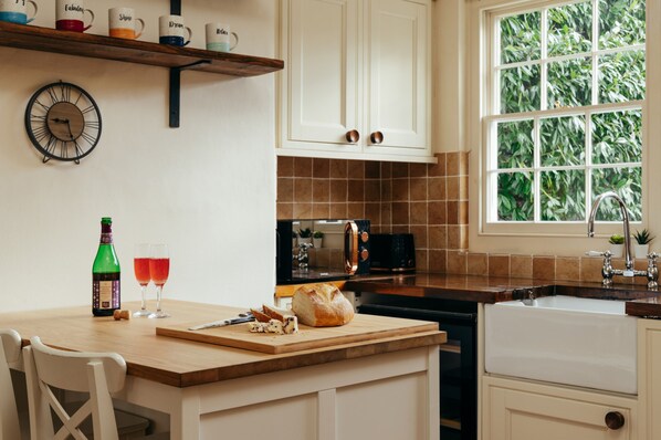 A kitchen with a wooden countertop, a loaf of bread, two glasses of red wine, a bottle of wine, and a clock on the wall. - Montpellier Cheltenham - Character Georgian Town House (Gloucestershire)