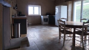 Een keuken met een raam, een koelkast, een fornuis en een eettafel met stoelen.