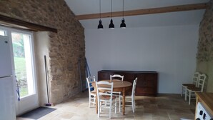 Een keuken met een stenen muur, een houten eettafel met stoelen, een wasmachine en hanglampen.