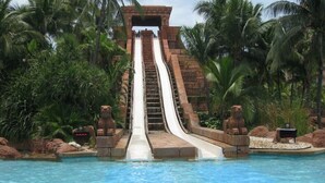 Eine Wasserrutsche mit Steinstruktur, umgeben von Palmen und einem Pool.