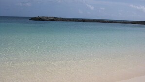 Ein Strand mit klarem türkisblauem Wasser und einem Felsen im Hintergrund.
