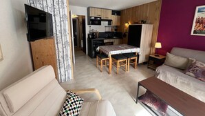 Een knus woongedeelte met een kitchenette, een eetgedeelte en een zithoek met een bank en een tafel.