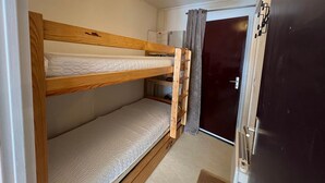 Een kleine kamer met twee stapelbedden, een plafondlamp in de vorm van een ster, een deur en een kleine koelkast.
