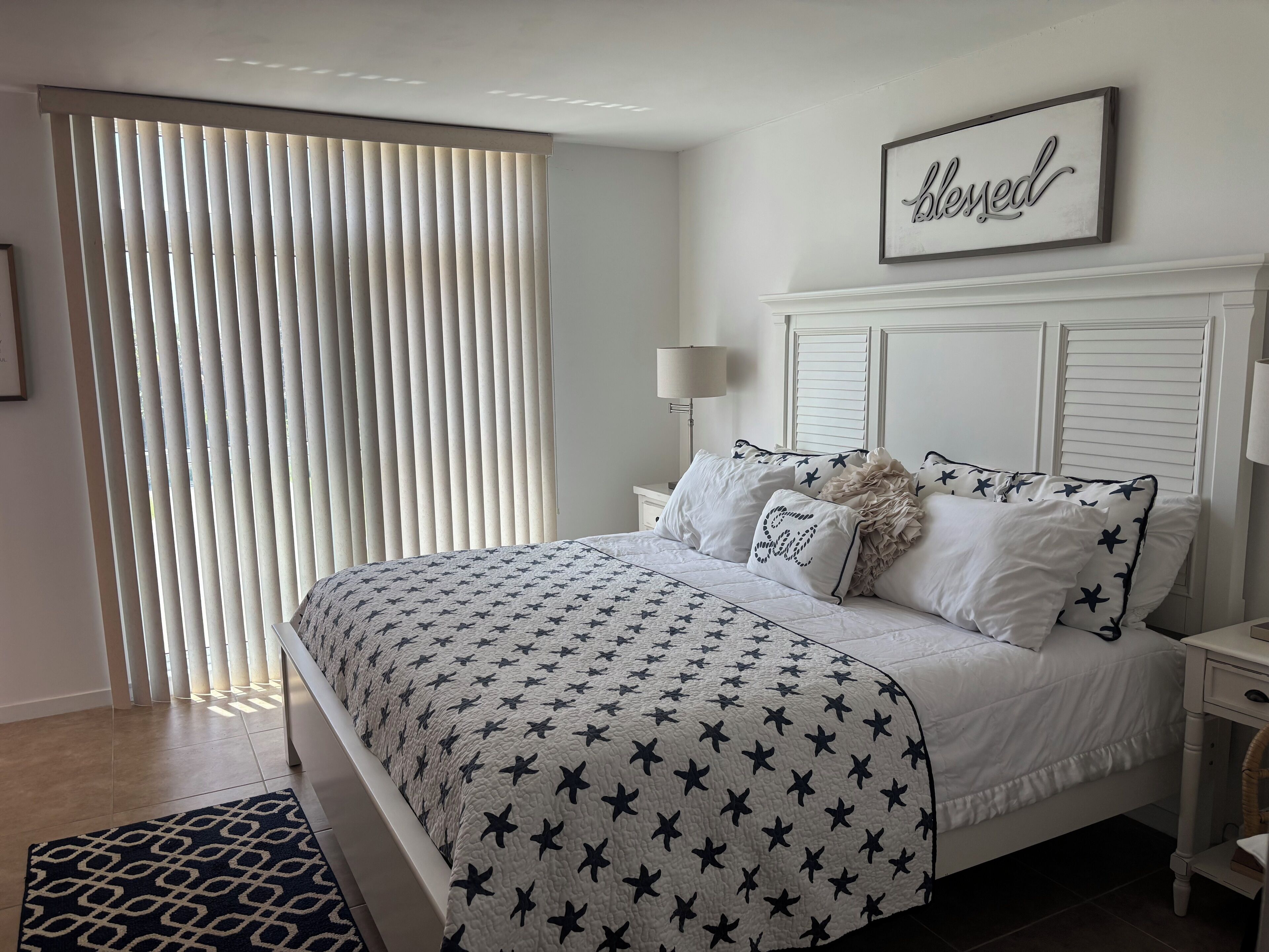 A bedroom with a bed, a bedside table, a lamp, and a window with blinds.