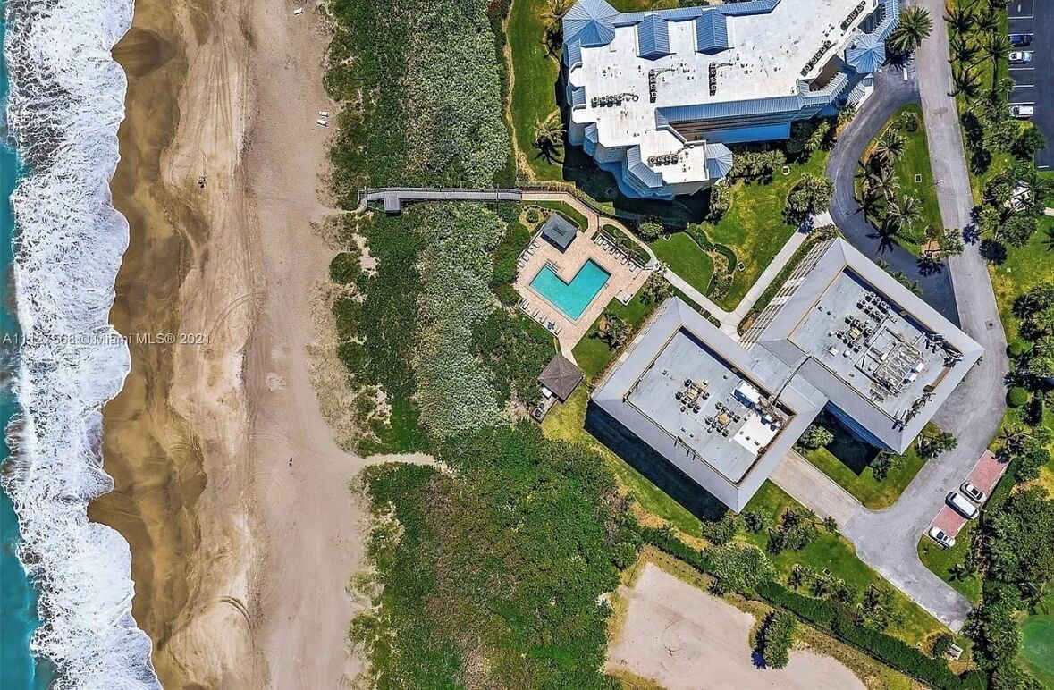 Vista aérea de una propiedad costera con playa, piscina y un edificio grande de diseño arquitectónico único.