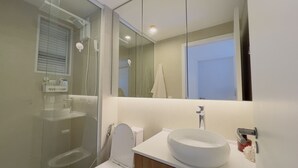 A modern bathroom with a glass shower enclosure, a white sink, and a large mirror. - Solarium Beach Club - Apartamento T1.304 (Itapoá)