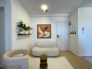 Uma sala de estar moderna com um sofá, uma poltrona, uma mesinha de madeira e uma estante suspensa com plantas.