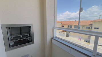 Uma varanda com guarda-corrimão branco, uma janela e vista para edifícios com telhados vermelhos.