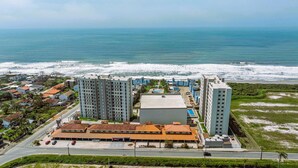 A coastal hotel with multiple high-rise buildings, a parking area, and a view of the ocean. - Solarium Beach Club - Apartamento T1.304 (Itapoá)
