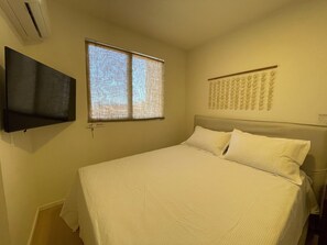 A bedroom with a bed, a television mounted on the wall, and a window with blinds. - Solarium Beach Club - Apartamento T1.304 (Itapoá)