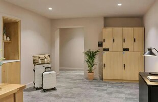 Ein Hotelzimmer mit Holzschrank, Schreibtisch mit Lampe, Blumentopf und zwei Koffern.