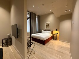 Ein modernes Hotelzimmer mit einem großen Bett, einem Flachbildfernseher, einem Schreibtisch mit Stuhl und einem Fenster mit Vorhängen.