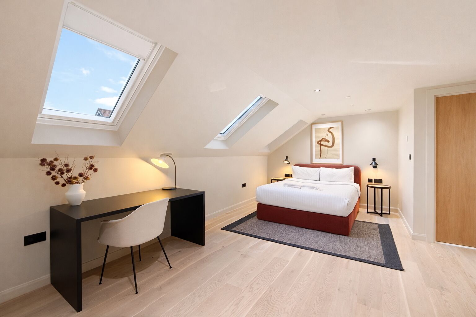 A bedroom with a skylight, a bed, a desk, and a chair.