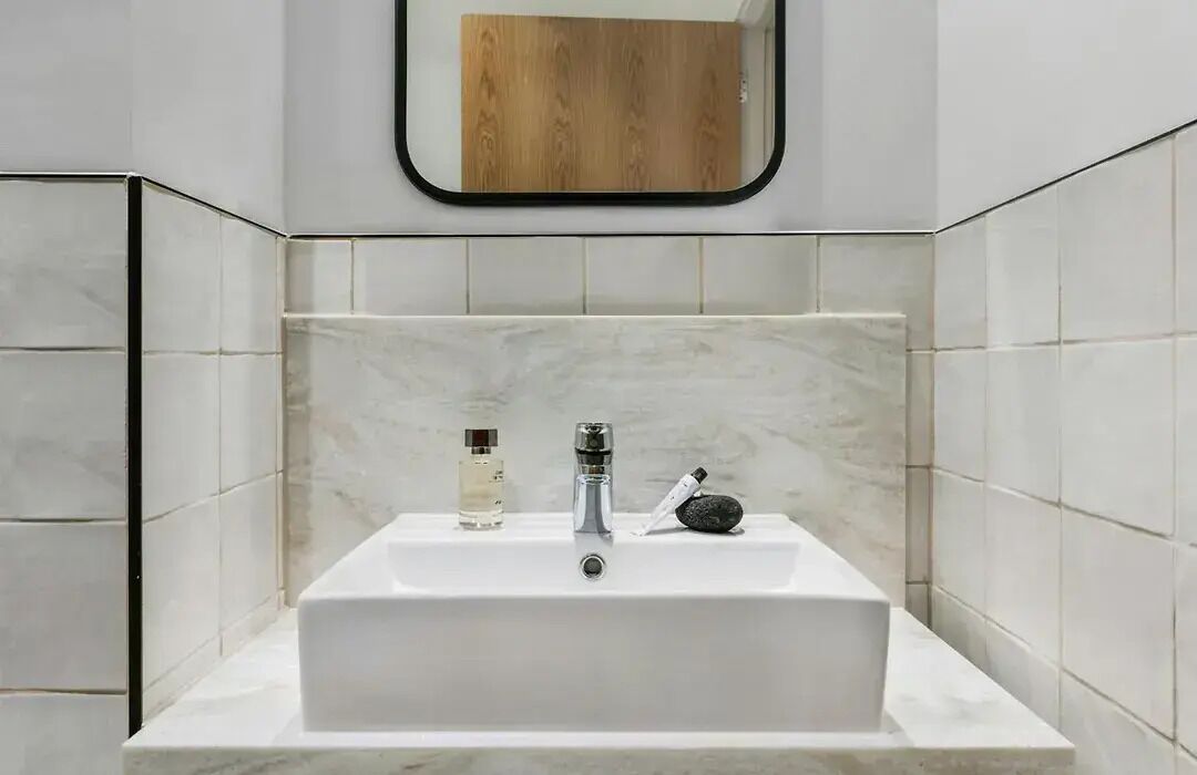 Un baño con un lavamanos blanco, un espejo y un panel de madera sobre el espejo.