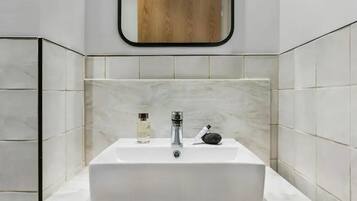 Un baño con un lavamanos blanco, un espejo y un panel de madera sobre el espejo.