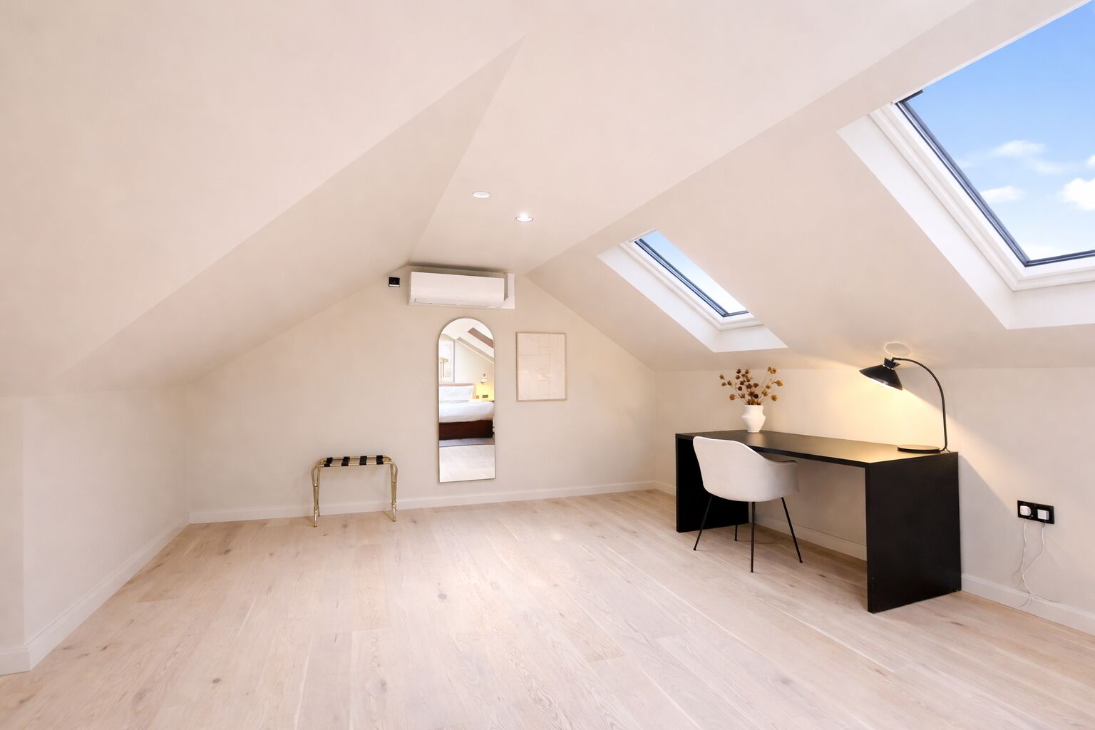 A modern loft bedroom with skylights, a desk, and a chair.