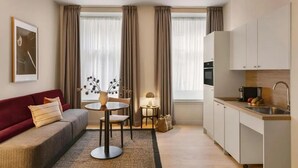 A modern hotel room with a sofa, dining table, and kitchenette.