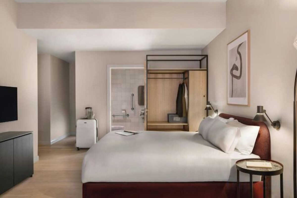 Habitación de hotel con cama, escritorio, televisor, armario y baño a la vista.
