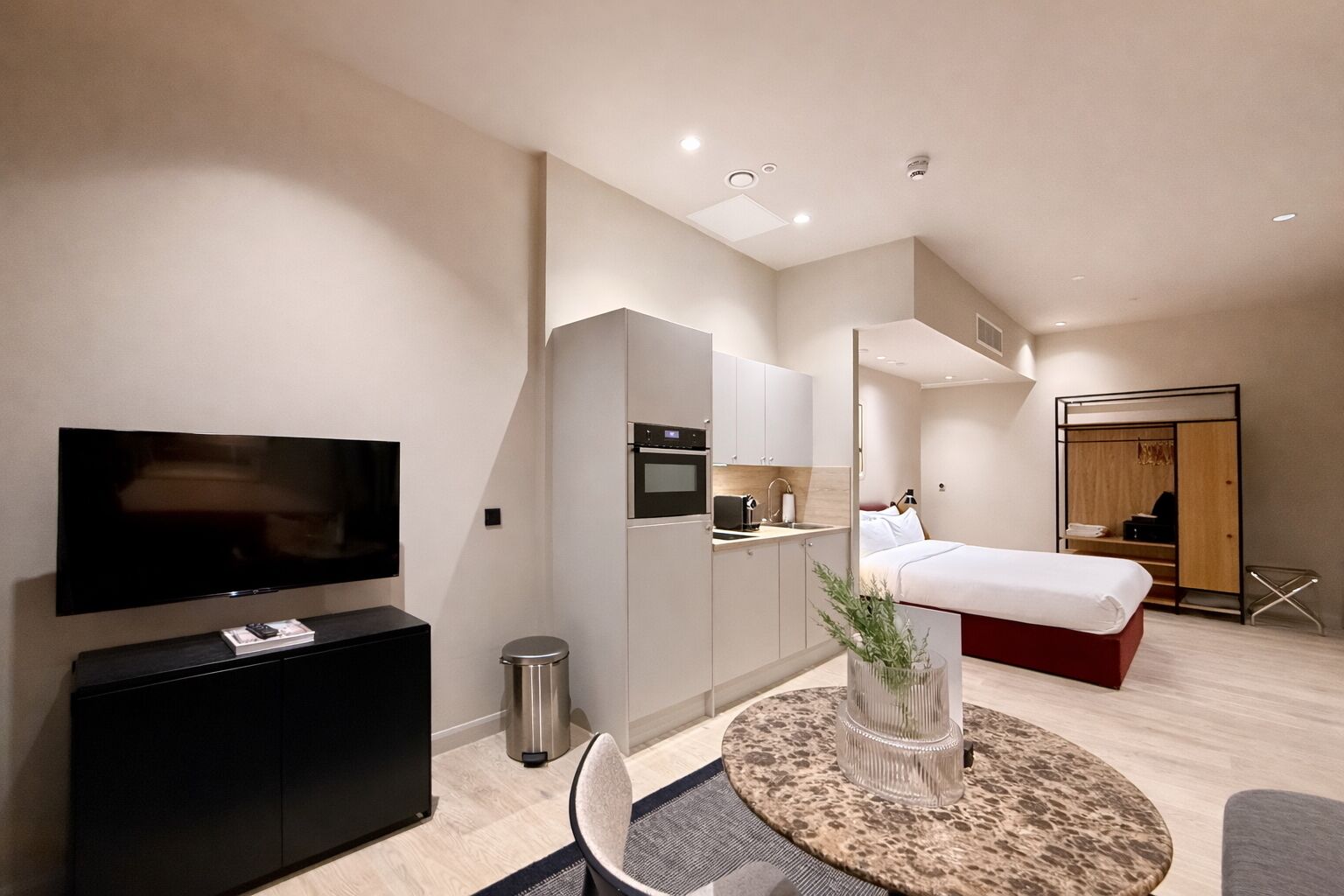 A modern hotel room with a flat-screen TV, kitchenette, bed, and a walk-in closet.