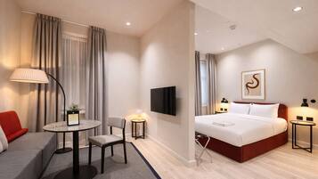 A hotel room with a bed, a TV, a desk with a chair, a sofa, and a lamp.