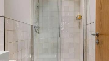 A shower with a glass door, a wooden door to the right, and a white tiled wall.