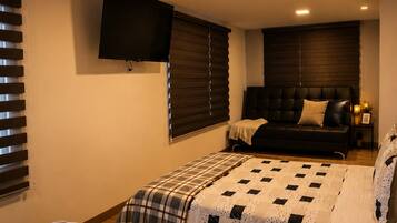 A bedroom with two beds, a TV mounted on the wall, and a window with blinds.