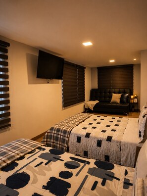 A bedroom with two beds, a TV mounted on the wall, and a window with blinds. - Modern Apartment Near Cuenca's Historic Center | Balcony • Garage • Pet-Friendly (Cuenca)