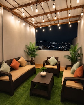 An outdoor seating area with sofas and a coffee table, surrounded by potted plants, under a pergola with string lights. - Modern Apartment Near Cuenca's Historic Center | Balcony • Garage • Pet-Friendly (Cuenca)