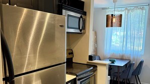 Eine moderne Küche mit Edelstahlgeräten, ein Essbereich mit Tisch und Stühlen sowie ein Fenster mit durchsichtigen Vorhängen.