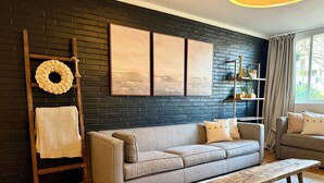 Ein Wohnzimmer mit einer dunkel verputzten Ziegelwand, einem grauen Sofa, einer Holzbank und einem weißen Teppich.